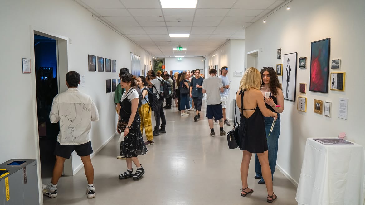 Busy graduation exhibition corridor with visitors and framed works on both walls