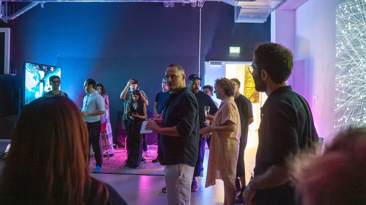 Dark audiovisual exhibition room with visitors, screens and projected artwork